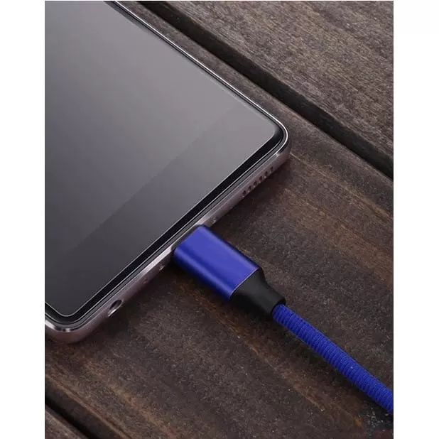Ein blaues Ladekabel wird in ein Smartphone auf einem Holztisch gesteckt.