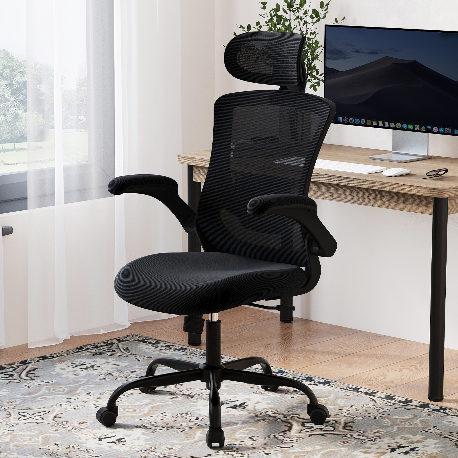Schwarzer Netzstuhl mit Kopfstütze vor einem Schreibtisch mit Computermonitor.
