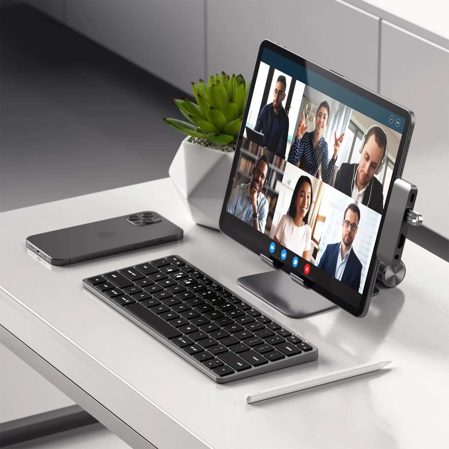 Tablet wyświetla rozmowę wideo z sześcioma osobami. Obok leżą smartfon, klawiatura i rysik.
