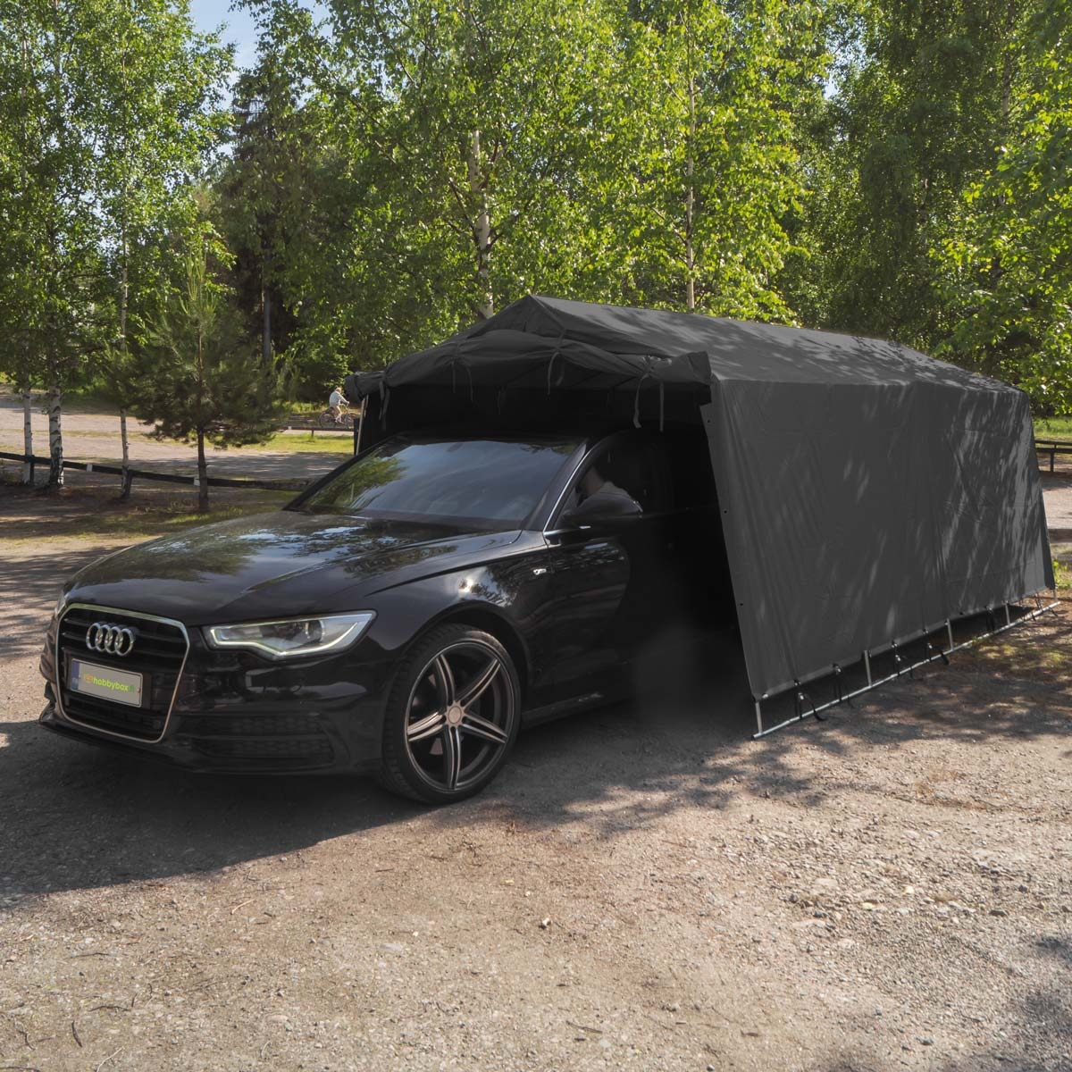 Ein schwarzer Audi unter einem grauen Zelt im Freien, umgeben von Bäumen.