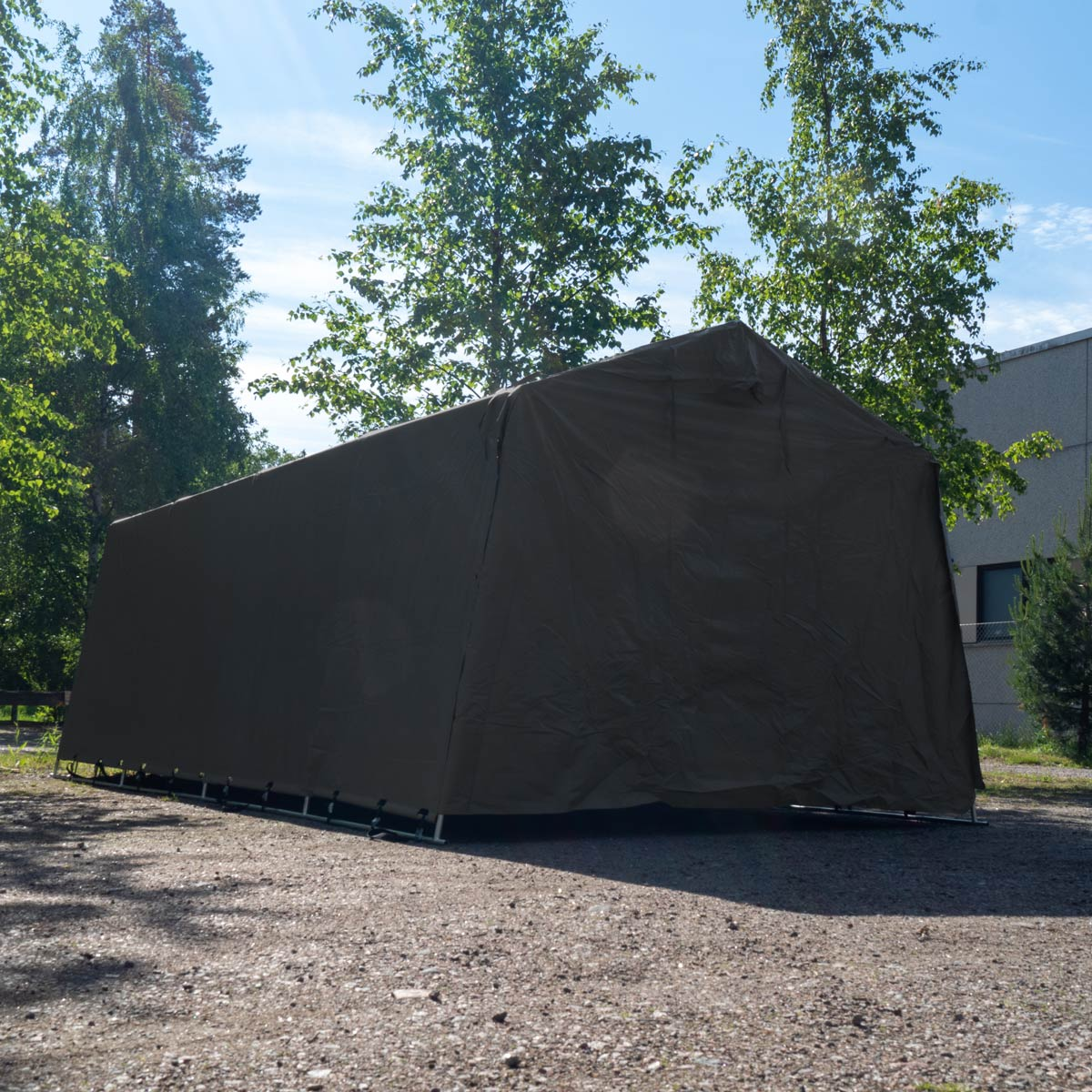 Eine große, dunkelgrüne, mit Plane abgedeckte Struktur mit Metallrahmen steht im Freien.