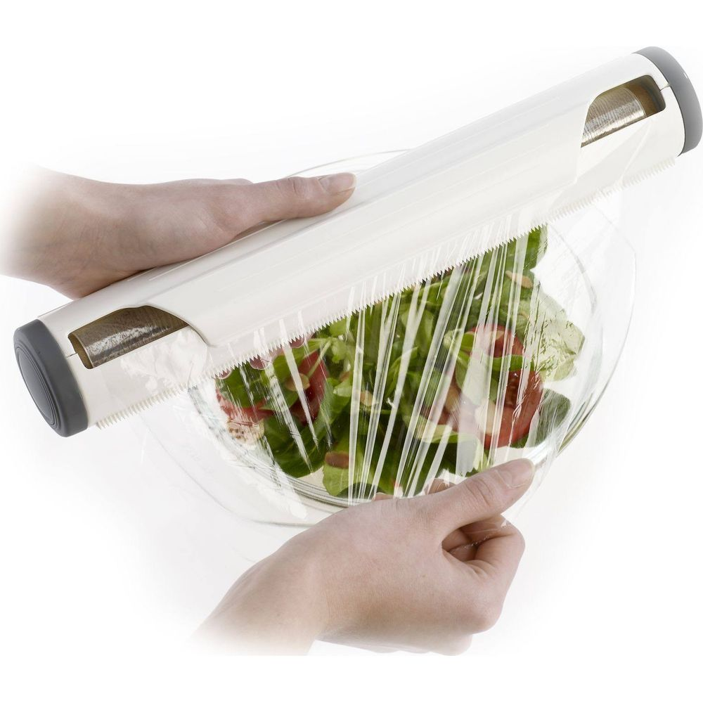 Le mani usano un dispenser bianco per avvolgere pellicola trasparente attorno a una ciotola di insalata.