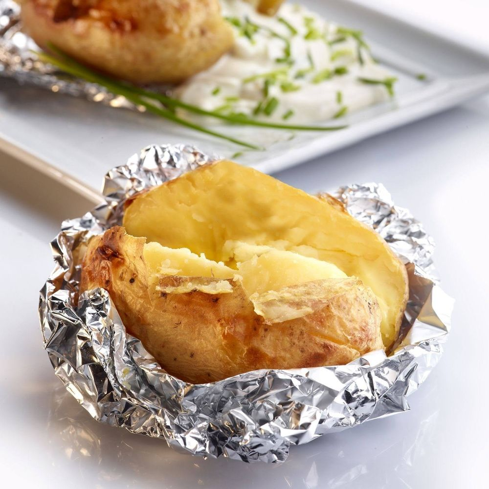 Una patata al forno in alluminio, con contorno di panna acida e erba cipollina.