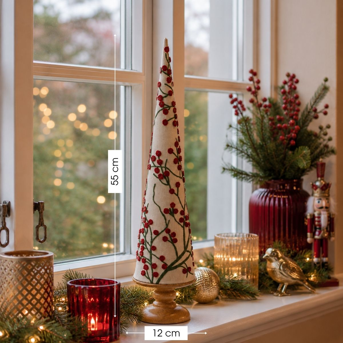 A festive cone tree with red berries, candle holders, a nutcracker, and string lights on a windowsill.
