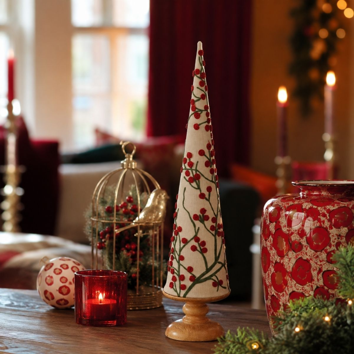 A decorative cone tree with red berries, a gold birdcage, and a red patterned vase.