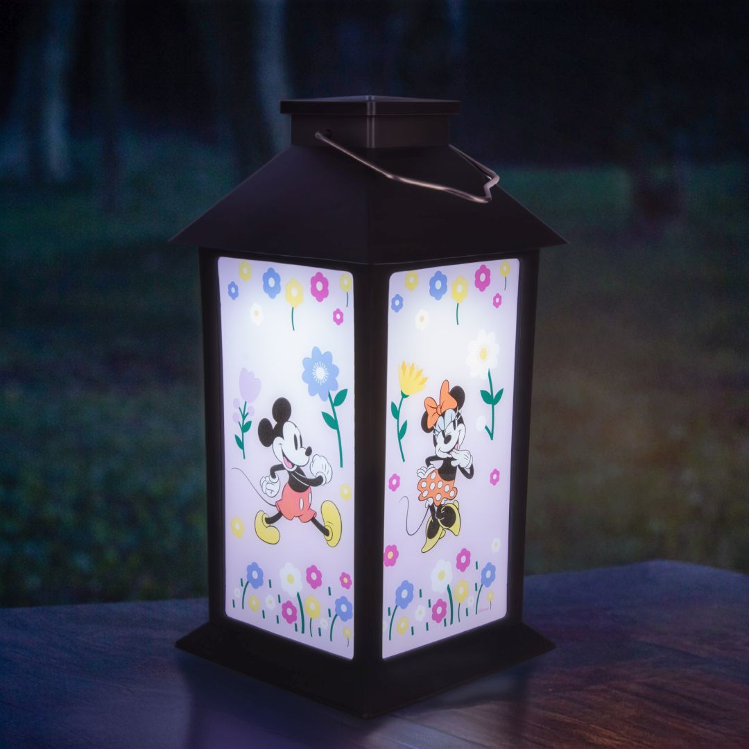 Latarnia solarna z Myszką Miki i Minnie, otoczona kolorowymi kwiatami.