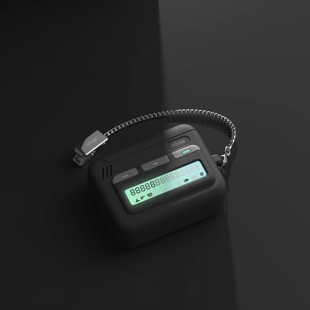 Czarny pager z srebrnym łańcuszkiem i świecącym ekranem na ciemnym tle.