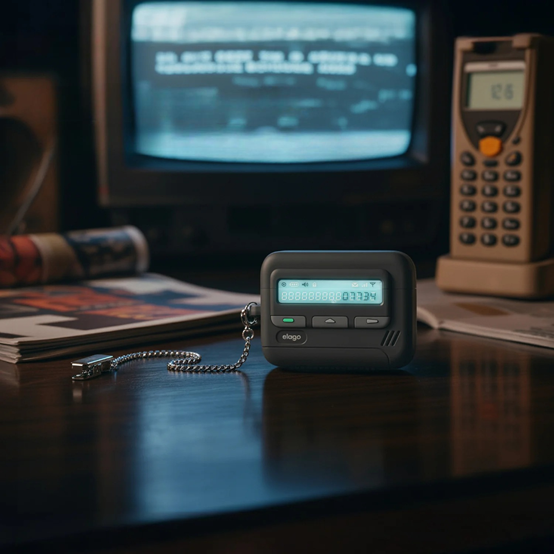 Czarny pager z łańcuchem leży na drewnianym stole przed starym telewizorem.