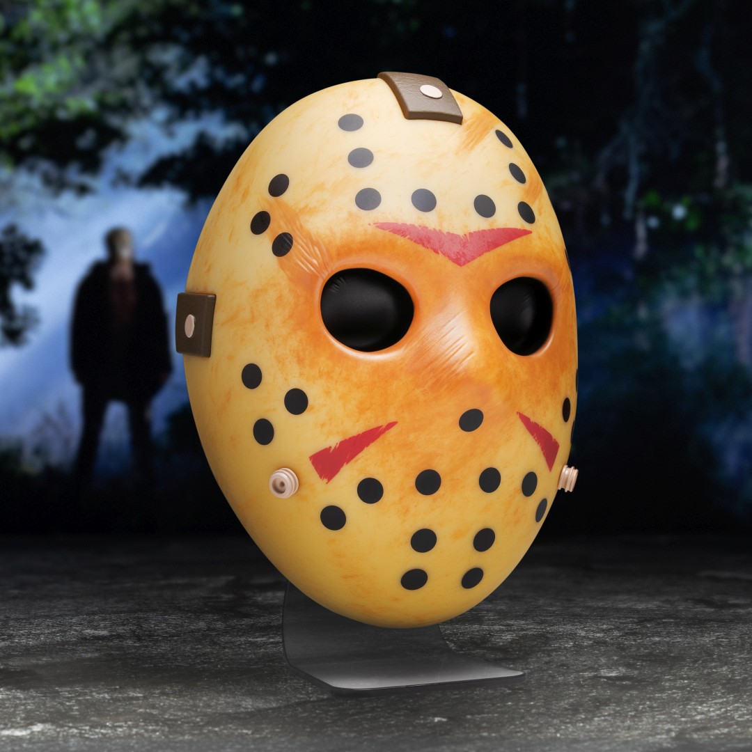 Gelbe Hockeymaske mit schwarzen Löchern und roten Markierungen, im Wald.