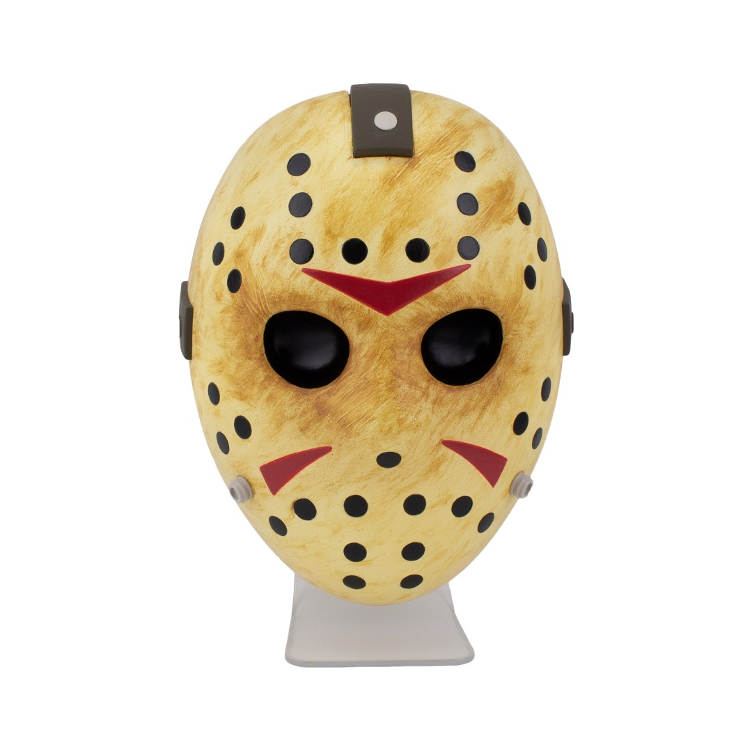 Eine gelbe Hockeymaske mit schwarzen Löchern und roten Dreiecken, auf einem Ständer.
