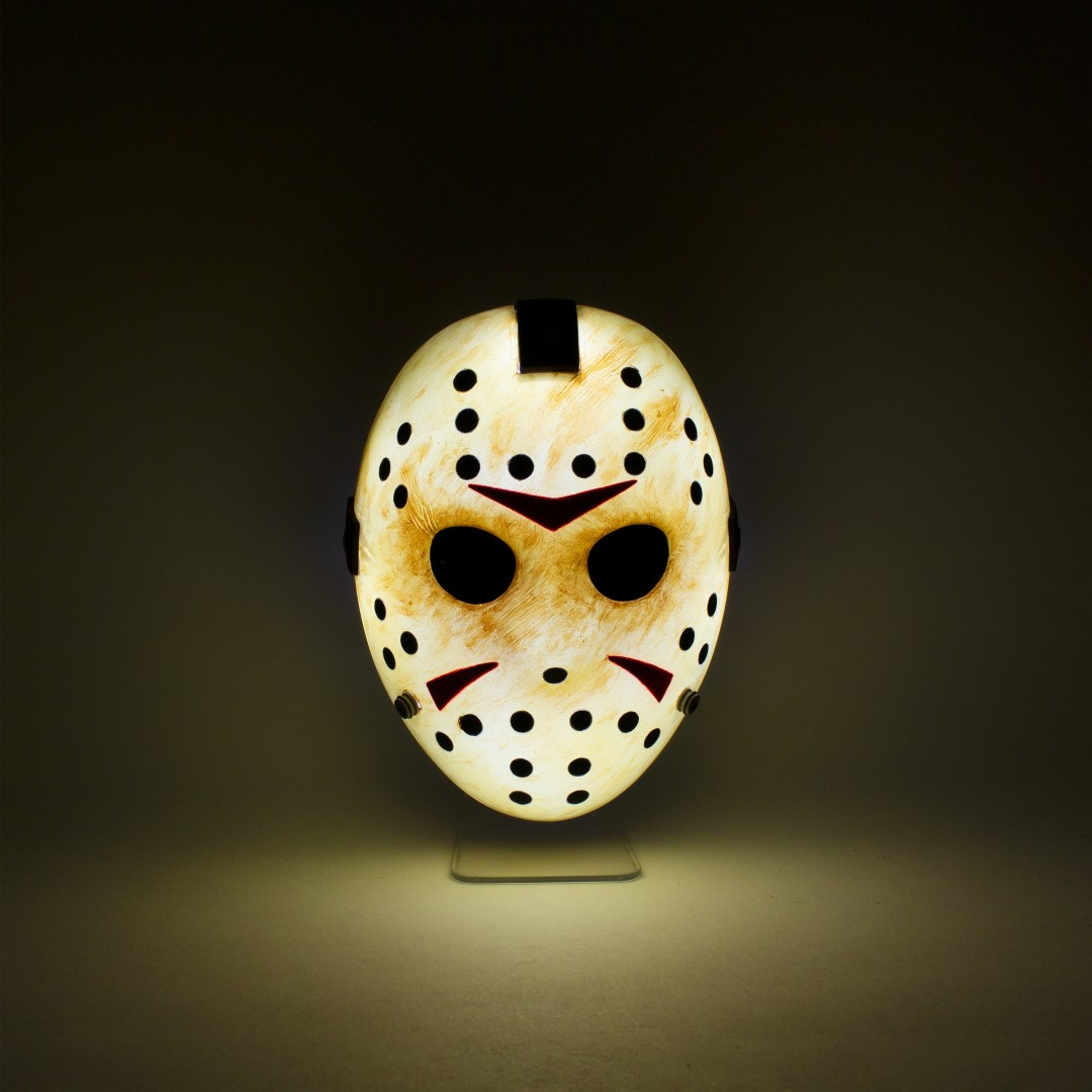 Eine weiße Hockeymaske mit schwarzen Löchern und roten Dreiecken, beleuchtet von hinten.