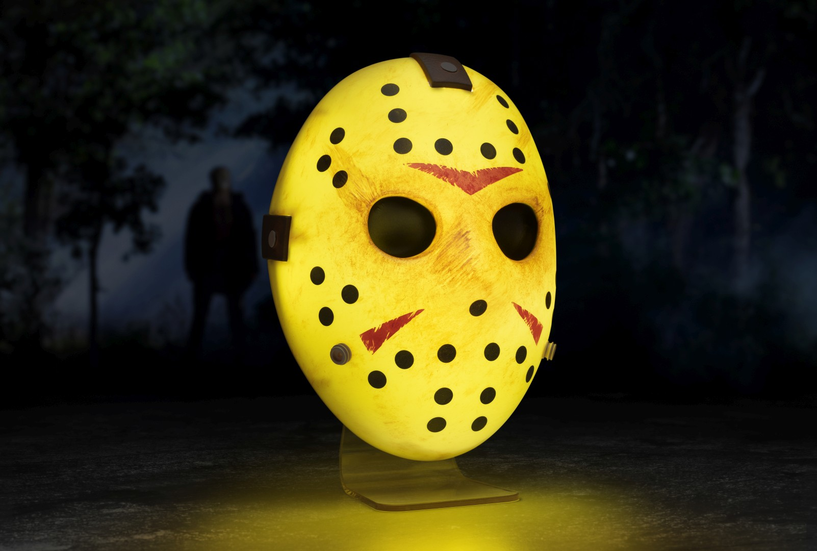 Eine gelbe Hockeymaske mit schwarzen Löchern und roten Markierungen auf einem Ständer.