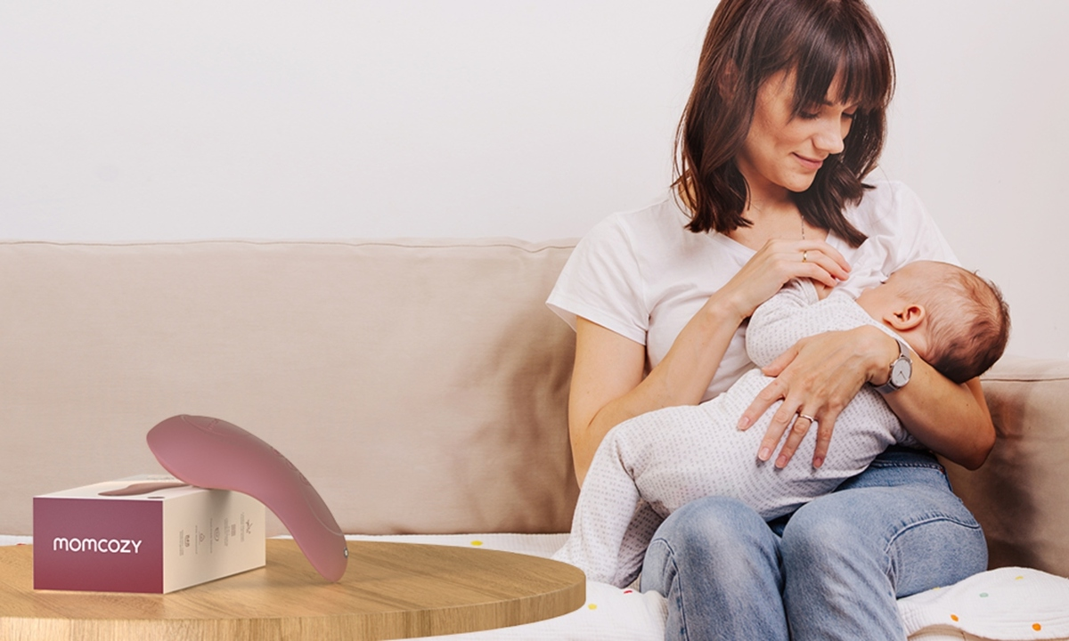 Una donna che allatta un bambino, con un dispositivo rosa nelle vicinanze.