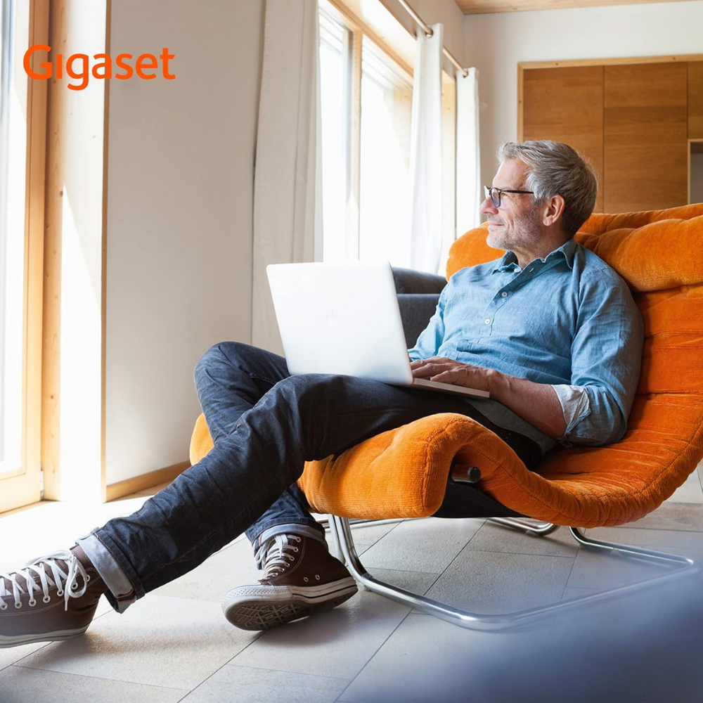 Ein Mann sitzt in einem orangefarbenen Sessel mit einem Laptop.
