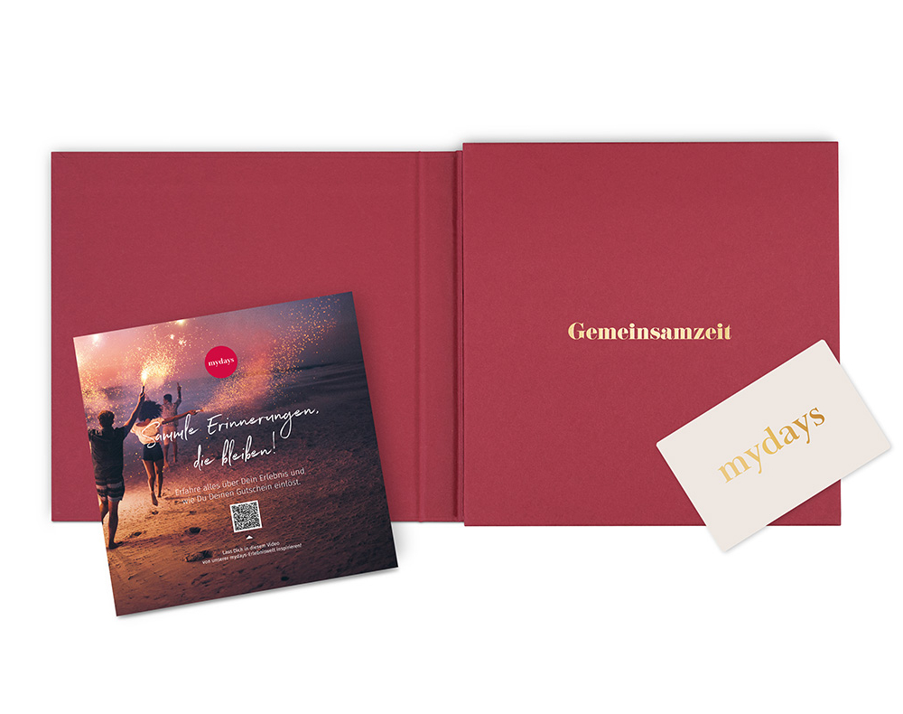 Rotes Buch mit Grußkarte. Links ein Flyer mit Feuerwerk und Menschen am Strand.