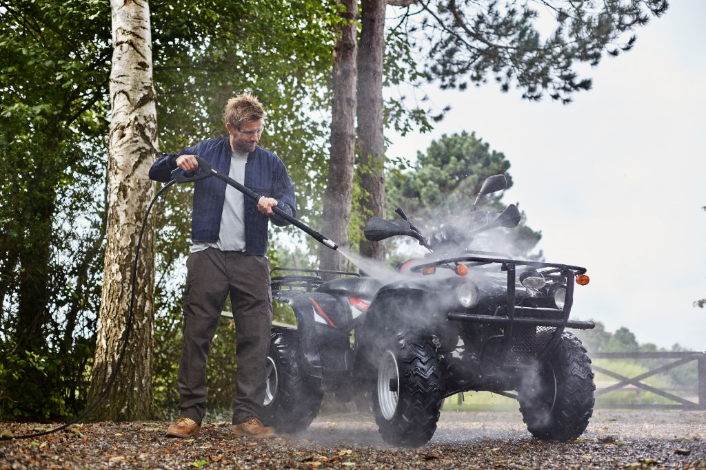 Uomo lava un quad ad alta pressione all'aperto.