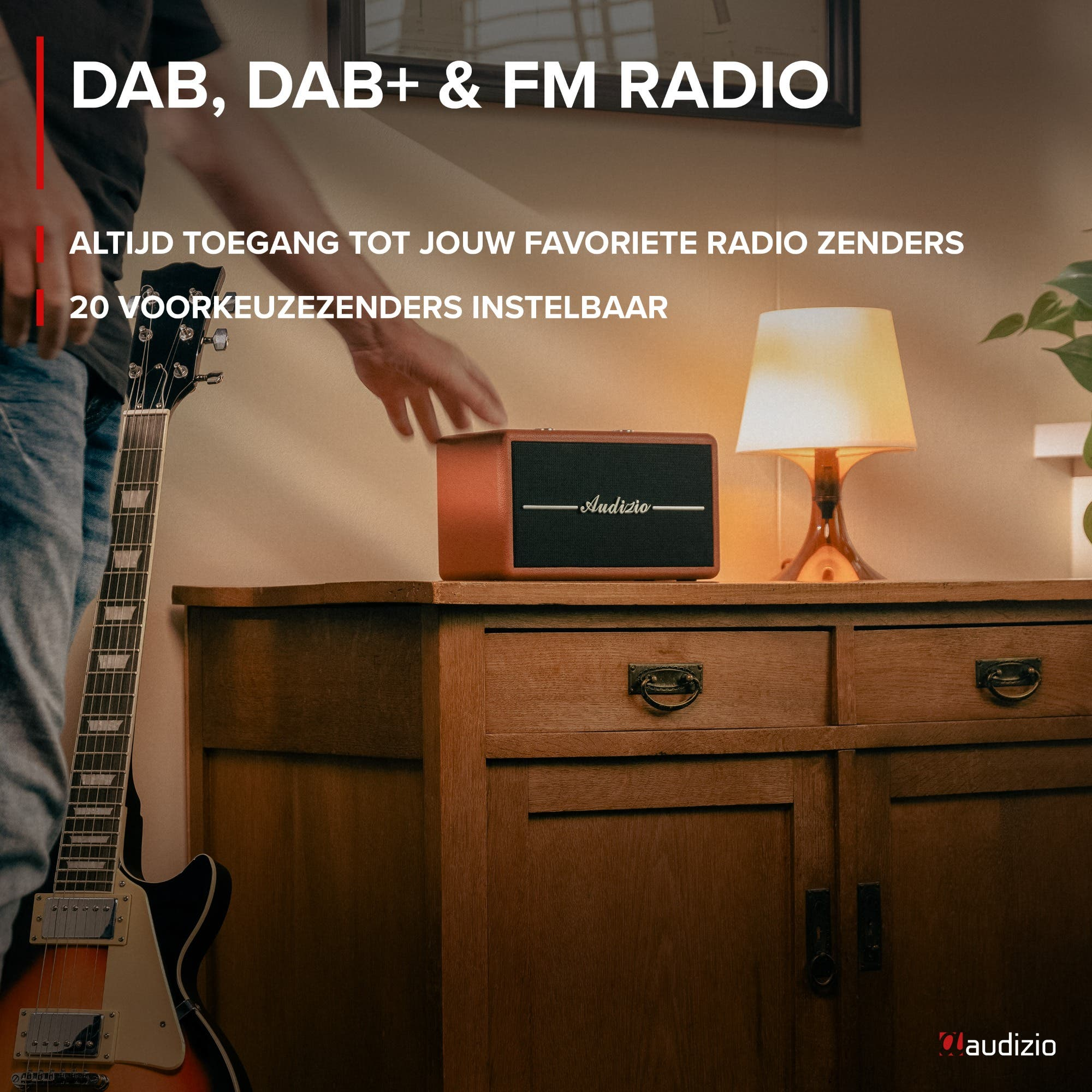 Un hombre agarra una radio Audizio marrón en un mueble de madera. Guitarra eléctrica al lado.