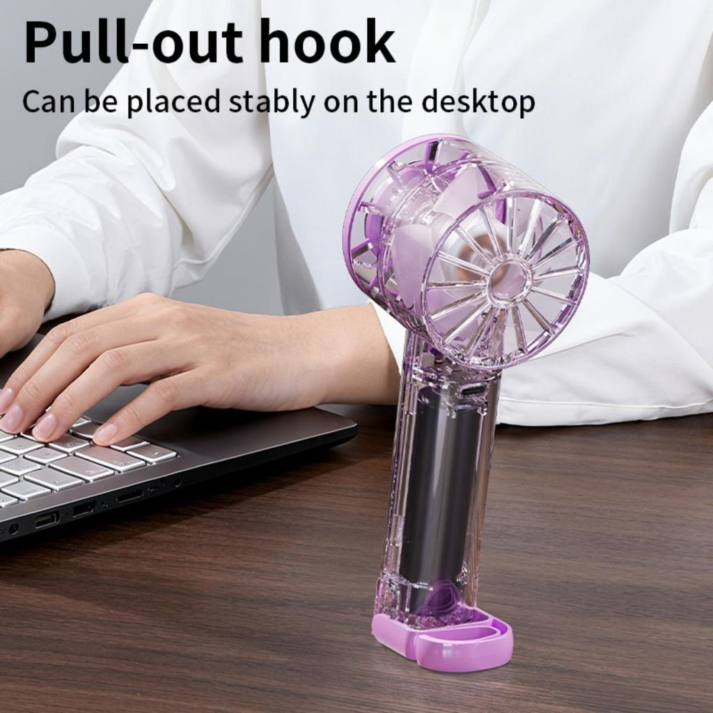 Eine Person tippt auf einem Laptop, ein violetter Ventilator steht daneben.