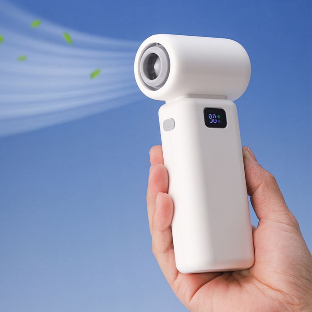 Ein weißer tragbarer Ventilator wird in einer Hand vor einem blauen Himmel mit wehenden grünen Blättern gehalten.