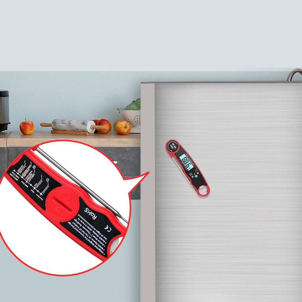 Ein rotes Digitalthermometer mit LCD-Anzeige klebt an einer Metalltür. daneben sind Äpfel und ein Nudelholz.