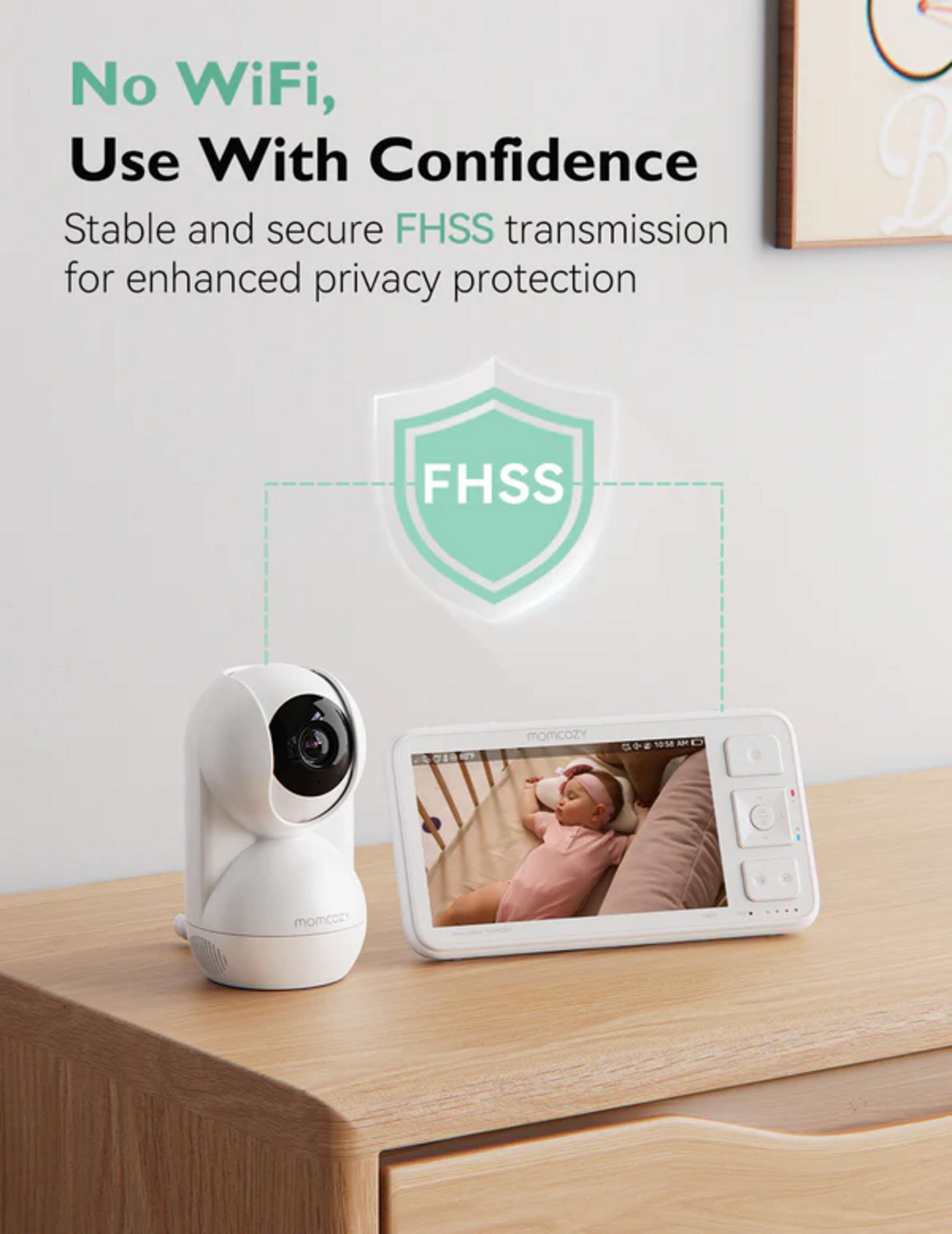 Ein weißer Babyfon-Monitor und eine Kamera auf einem Holztisch. Das Display zeigt ein Baby.
