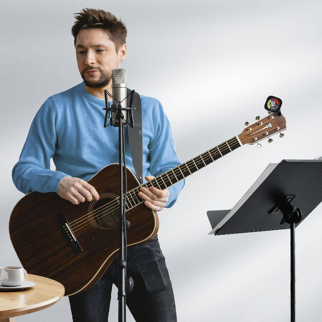 Ein Mann spielt Akustikgitarre vor einem Mikrofon, Notenständer und Kaffee.