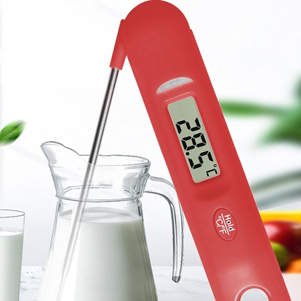 Ein rotes Digitalthermometer misst die Temperatur von Milch in einer Glaskaraffe.