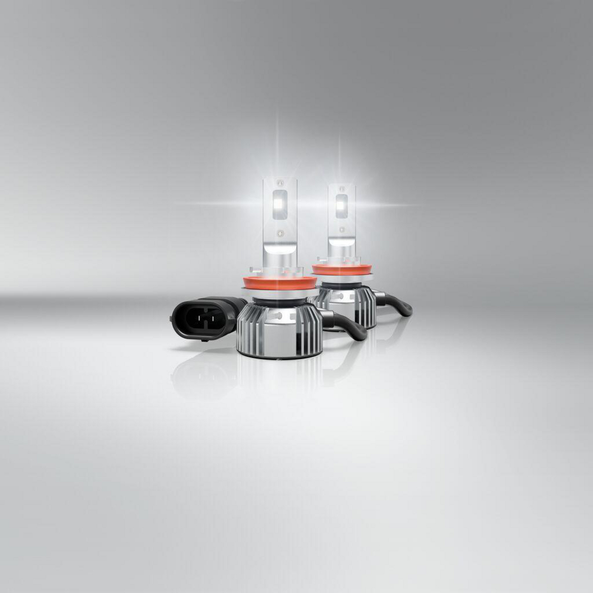 Zwei silberne LED-Autolampen mit orangefarbenen Ringen und Kabeln auf grauem Hintergrund.