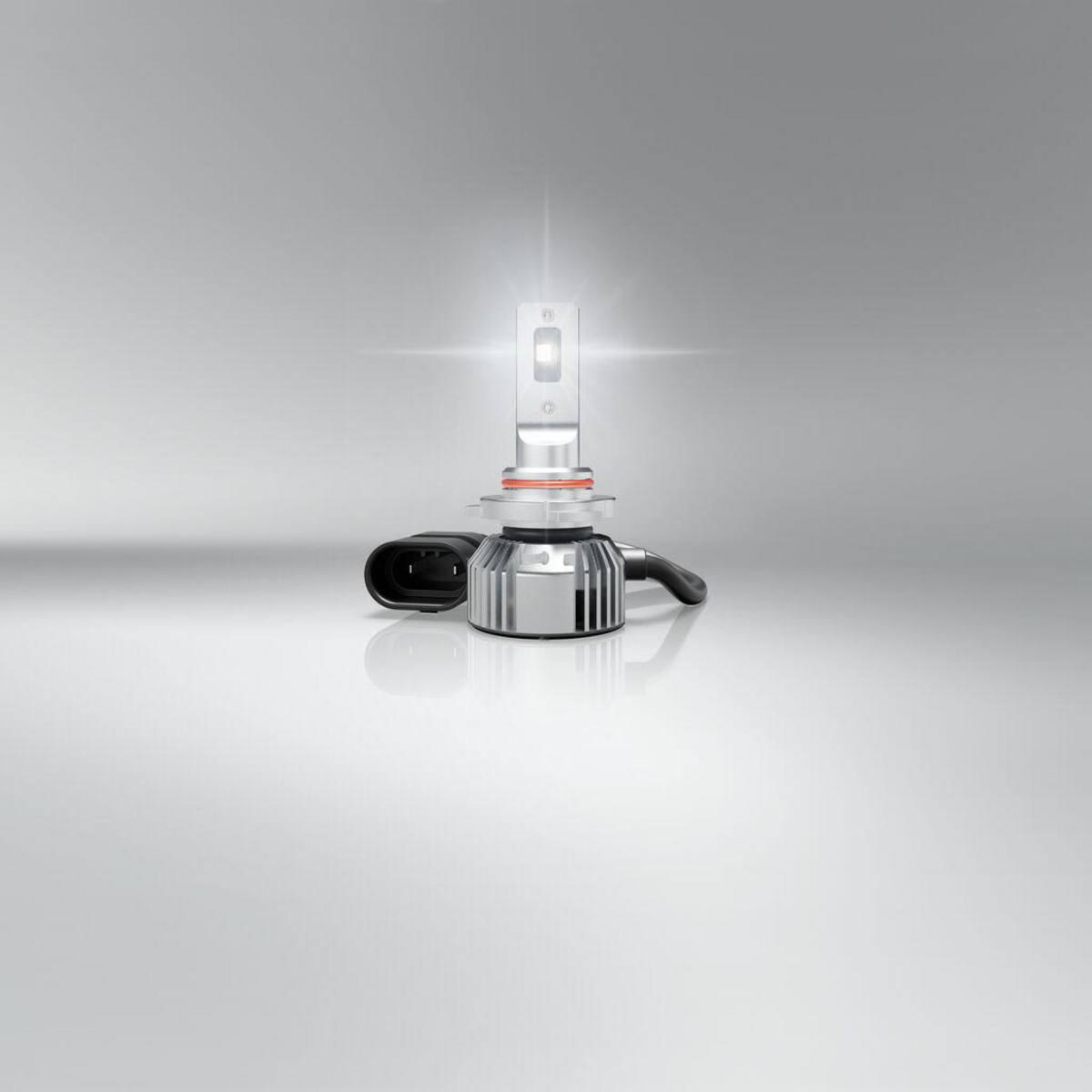 Ein silberner LED-Scheinwerfer mit schwarzem Stecker steht auf einem spiegelnden grauen Hintergrund.