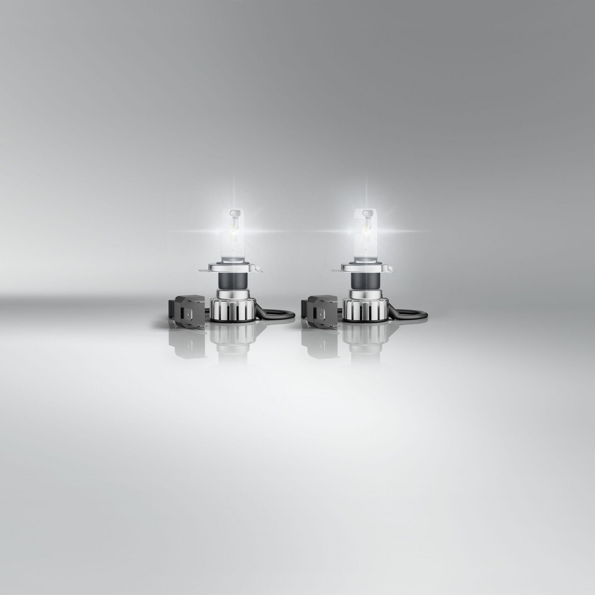 Zwei H4-Autolampen auf reflektierender Oberfläche, mit Lichterschein.