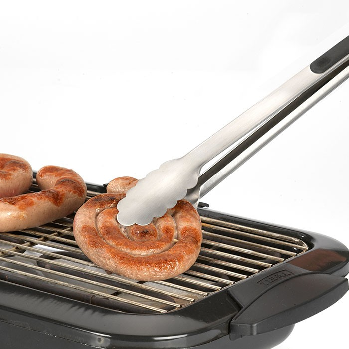 Eine Silberzange wendet eine spiralförmige Bratwurst auf einem Grill.