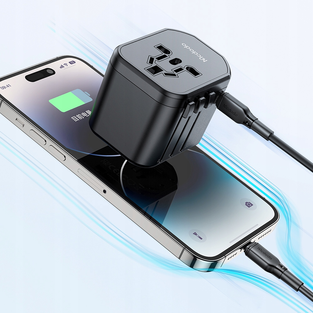Ein schwarzer Reiseadapter lädt ein Smartphone auf, das auf einem Tisch liegt.