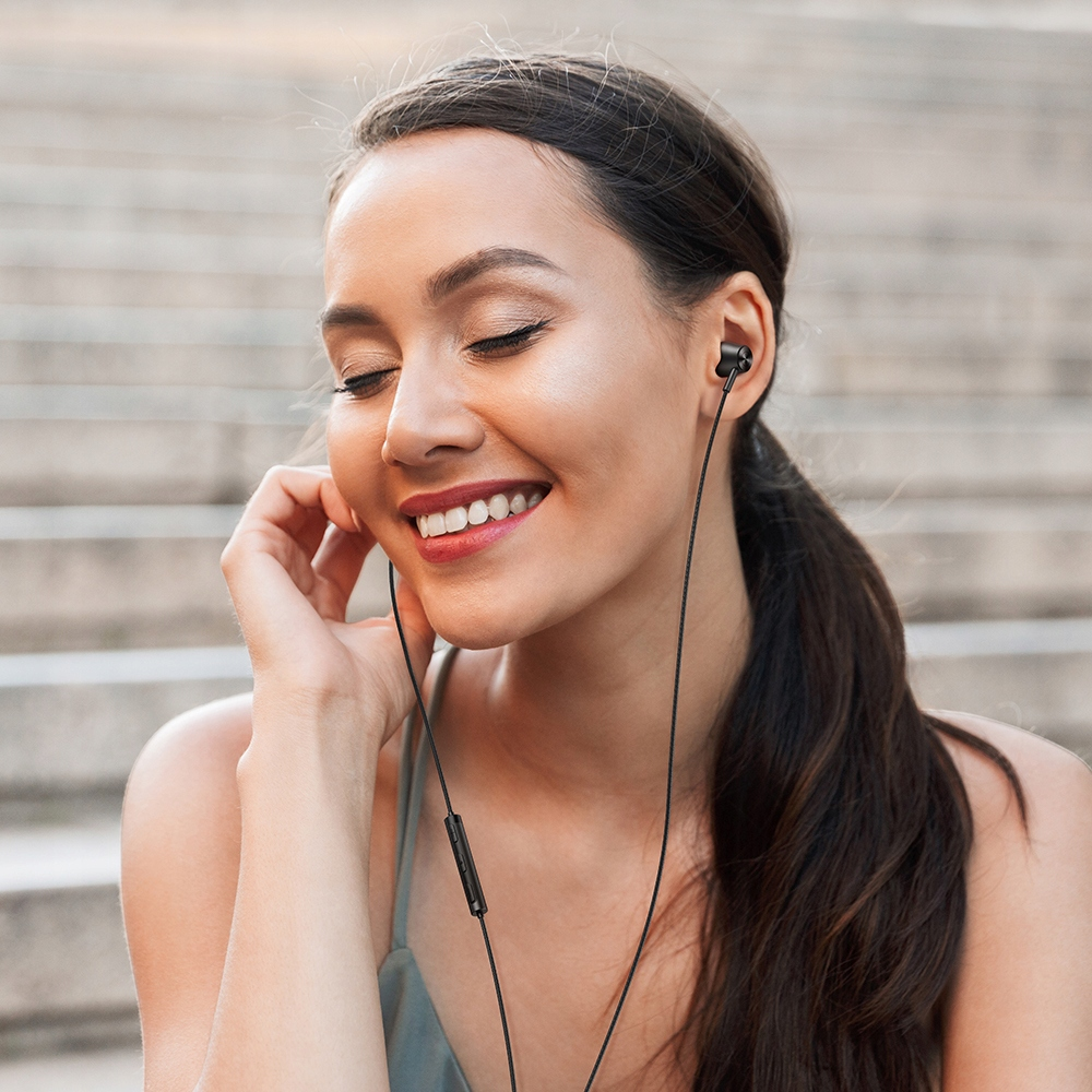 Una donna con auricolari sorride a occhi chiusi su gradini di pietra.