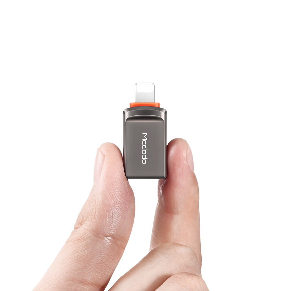Eine Hand hält einen kleinen grauen Adapter mit orangem Akzent.