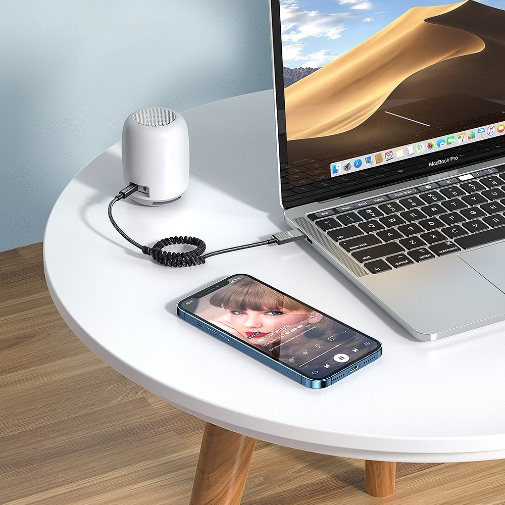Ein weißer Mini-Lautsprecher ist über ein Kabel mit einem Laptop verbunden. Daneben liegt ein Smartphone.