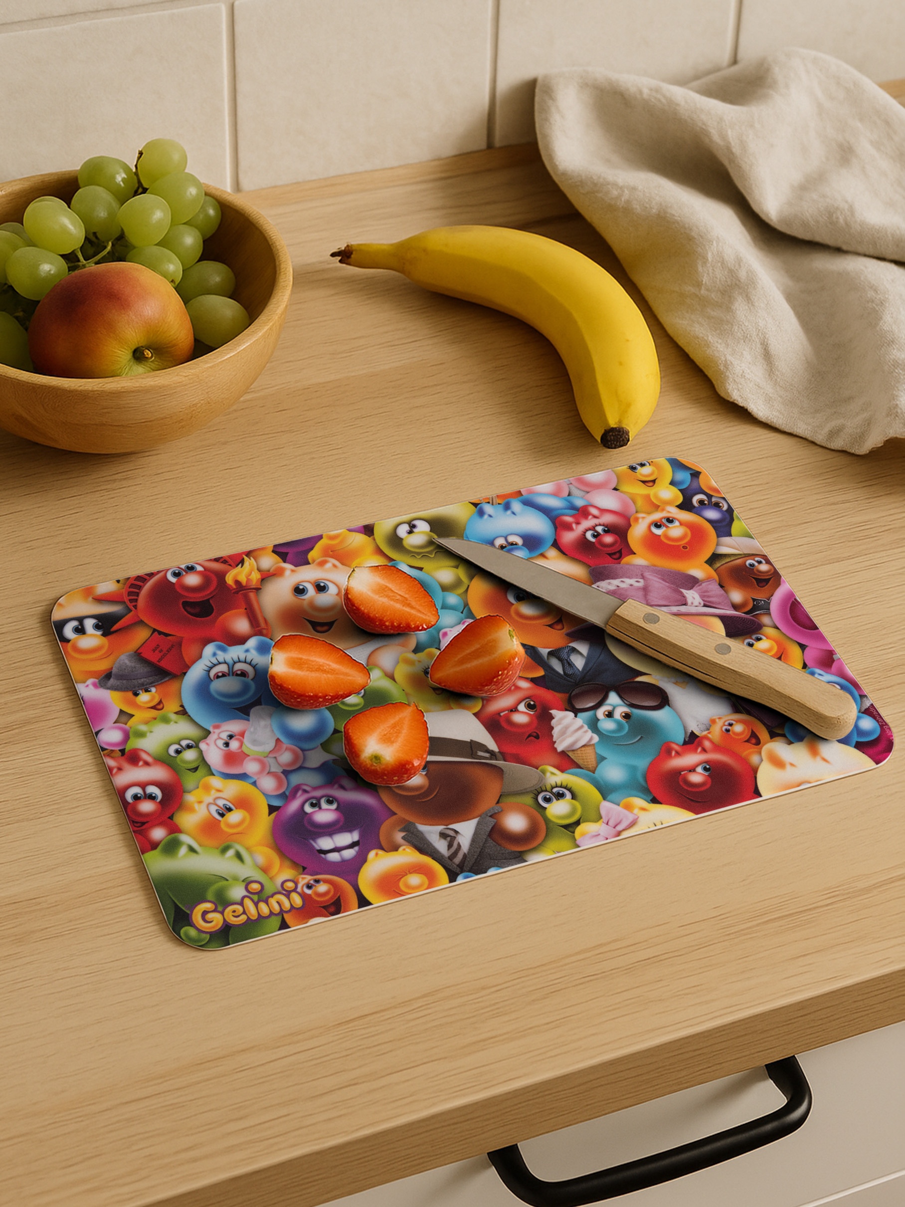 Buntes Schneidebrett mit Comicfiguren, Erdbeeren, Banane, Apfel und Trauben.
