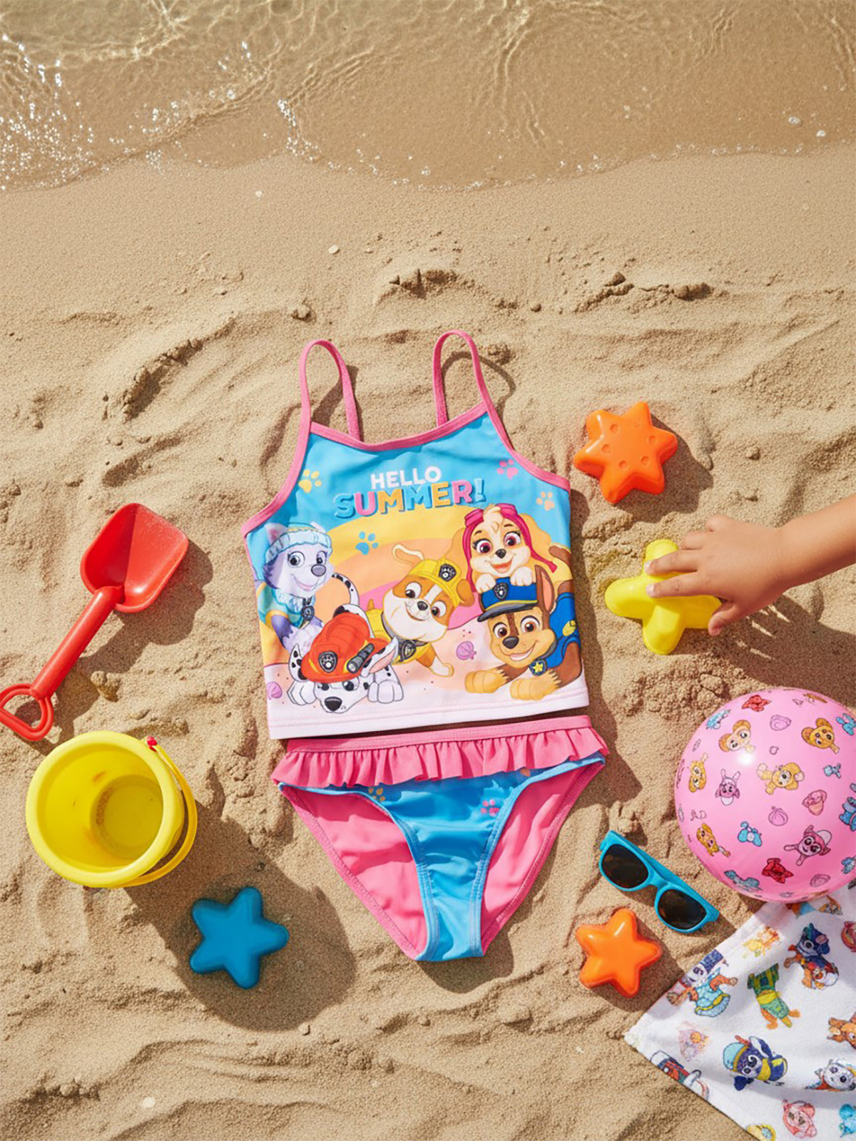 Paw Patrol Badeanzug am Strand mit Spielzeug, Schaufel, Eimer und Ball.
