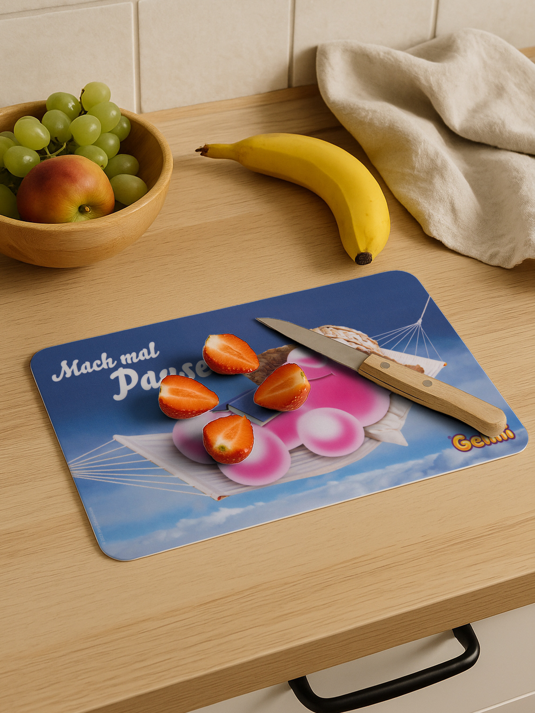Ein Messer liegt auf einem Schneidebrett mit Erdbeeren, Banane, Trauben und Apfel.