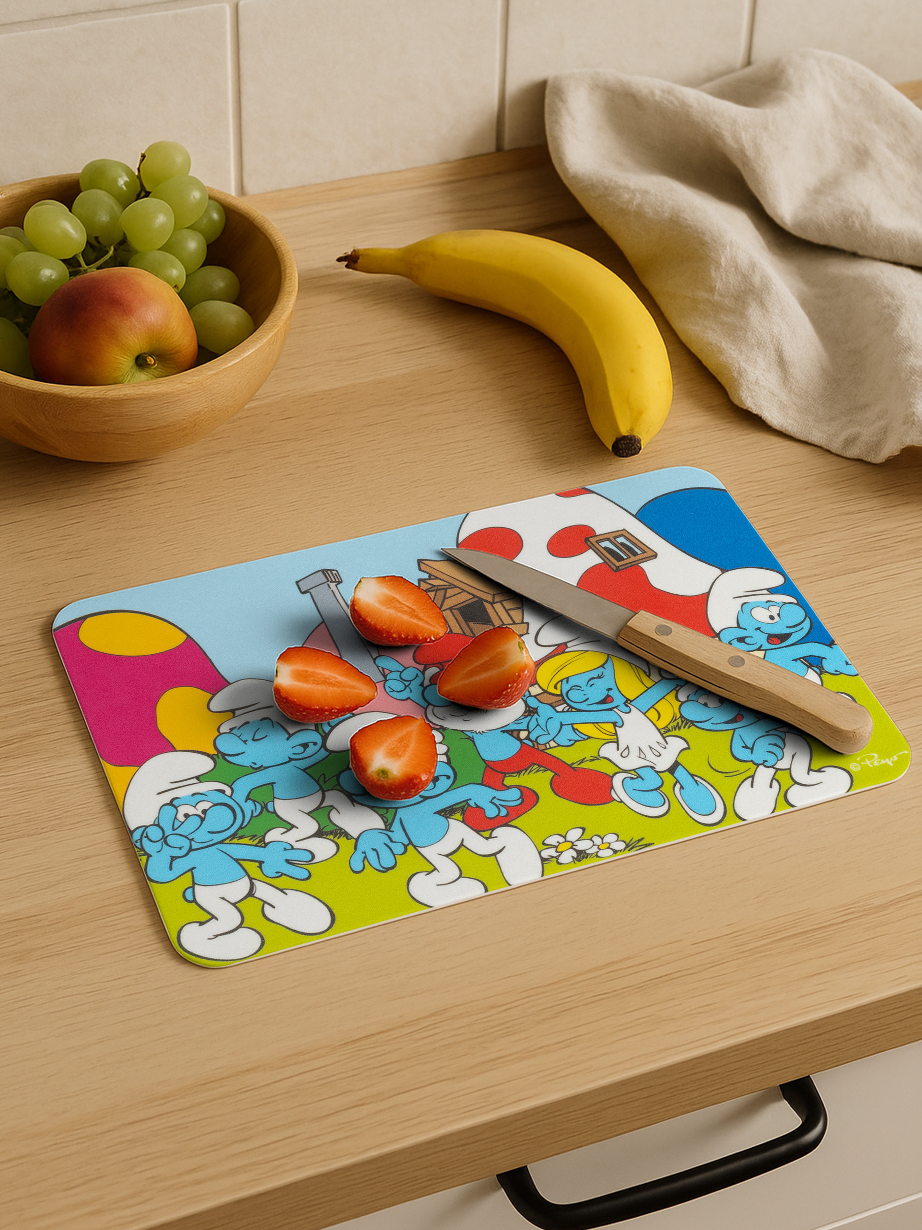 Schnittbrett mit Schlümpfen, Erdbeeren, Banane und Obst in einer Schale.