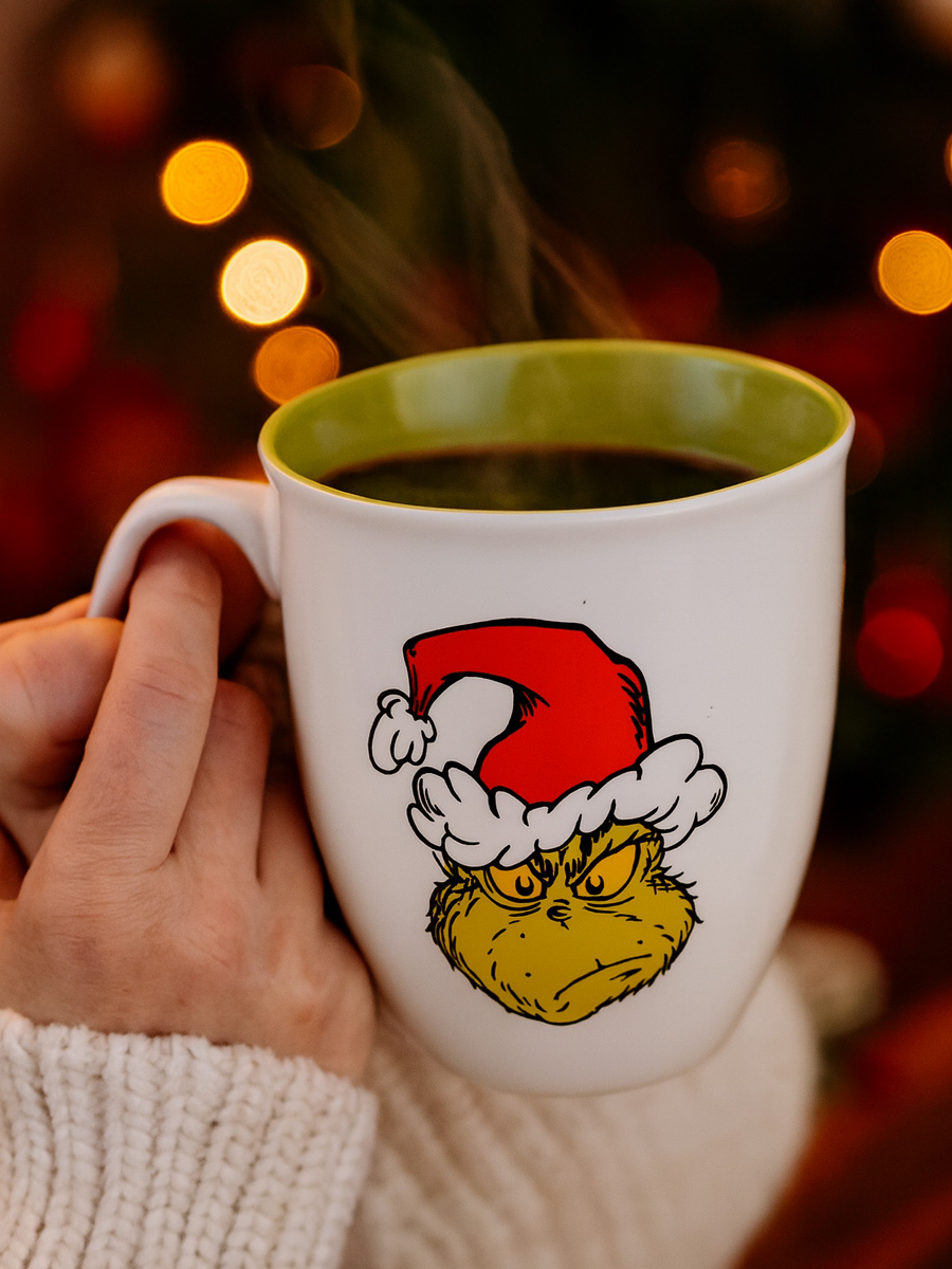 Eine Tasse mit dem Grinch-Gesicht und Weihnachtsmannmütze, dampfend heiß.