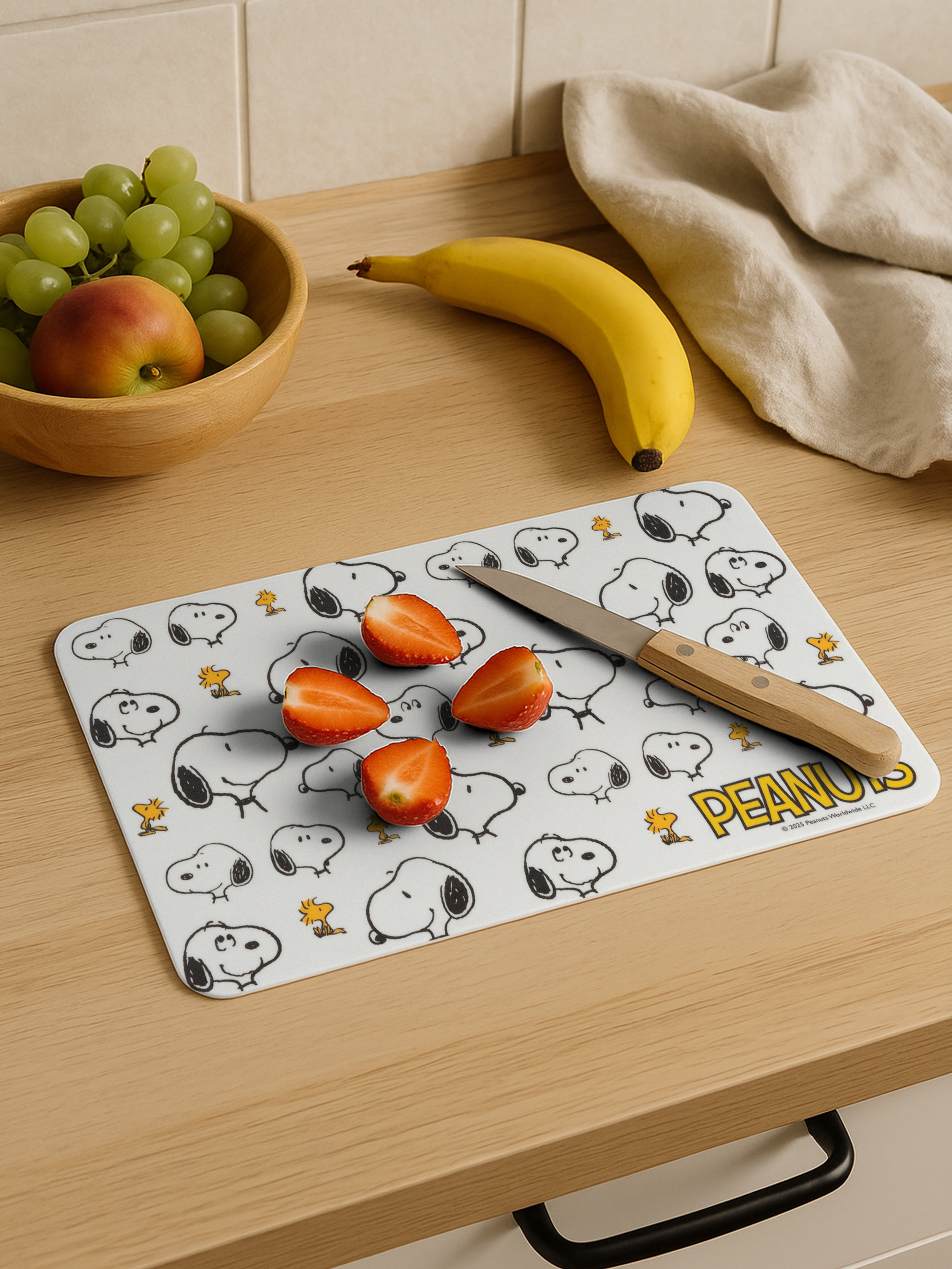 Schneidebrett mit Snoopy-Motiv, Erdbeeren, Banane, Apfel und Trauben.