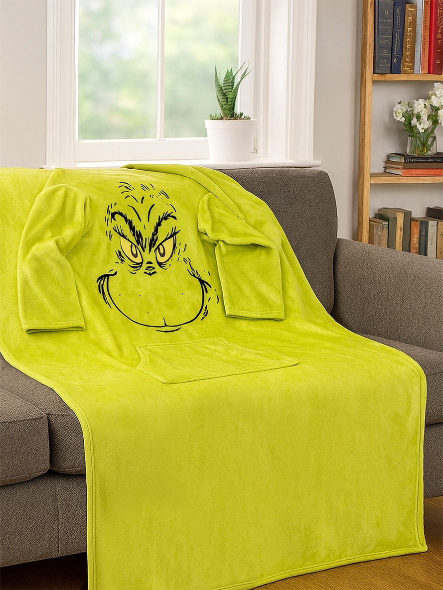 Eine leuchtend grüne Decke mit dem Grinch-Gesicht und Armen liegt auf einem Sofa.