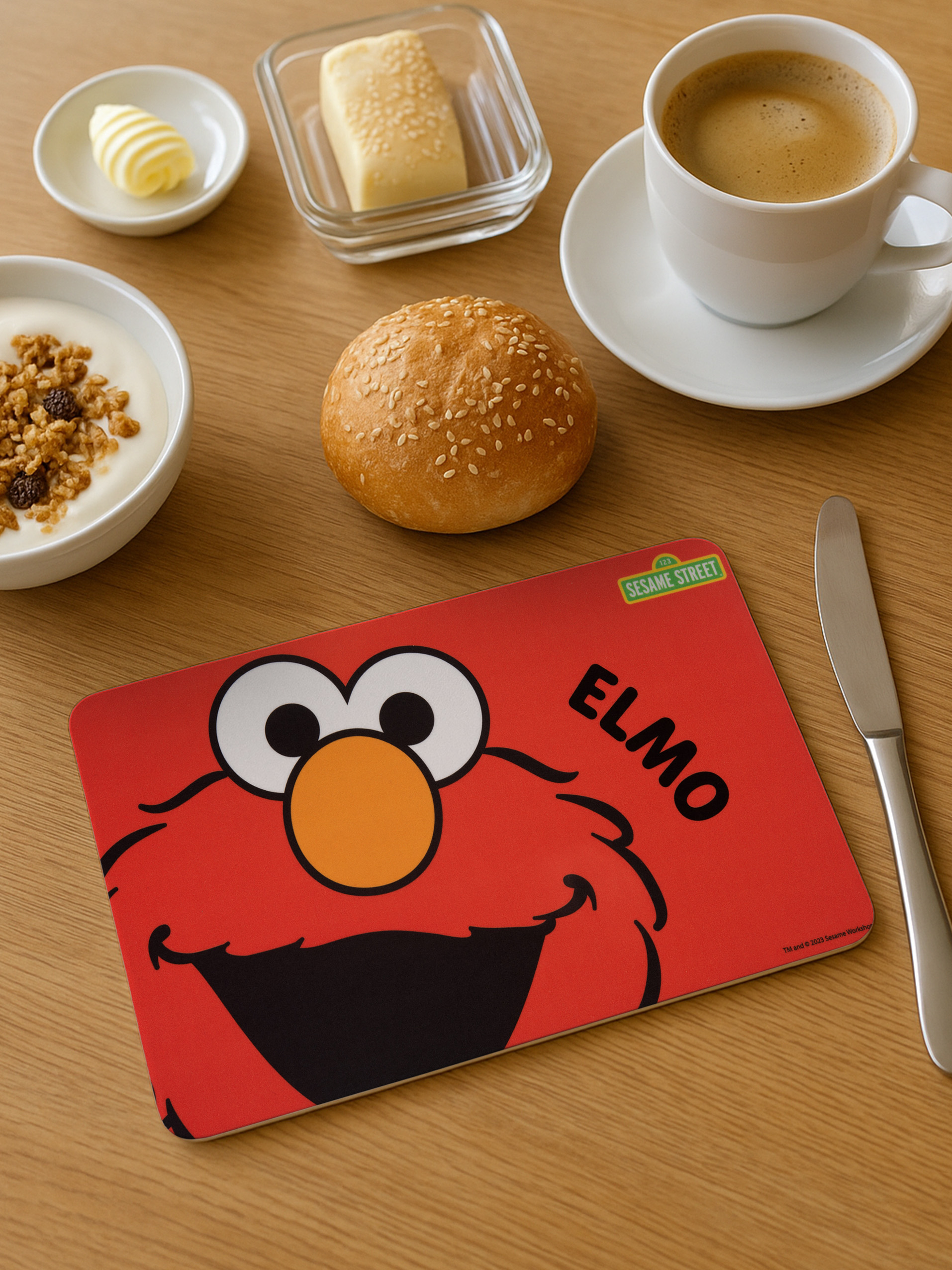 Frühstückstisch mit Joghurt, Brötchen, Butter, Kaffee und Elmo-Matte.