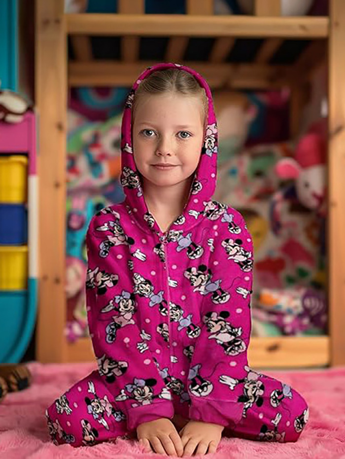 Ein kleines Mädchen in einem pinken Schlafanzug mit Minnie-Maus-Motiv sitzt auf einem Teppich.
