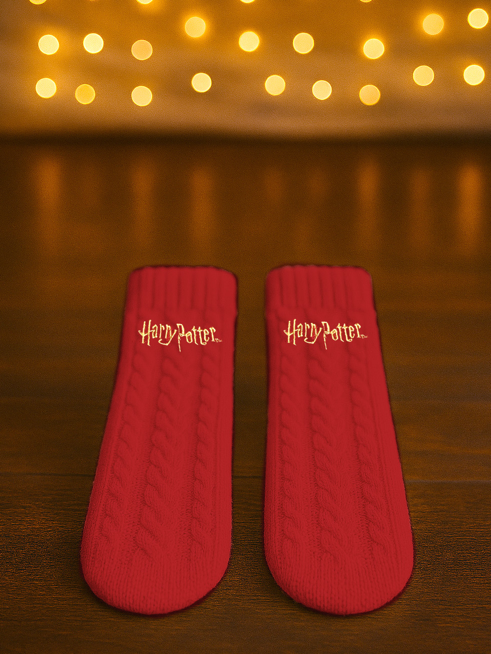 Zwei rote Harry Potter Socken mit Zopfmuster auf Holzuntergrund mit Bokeh-Lichtern.