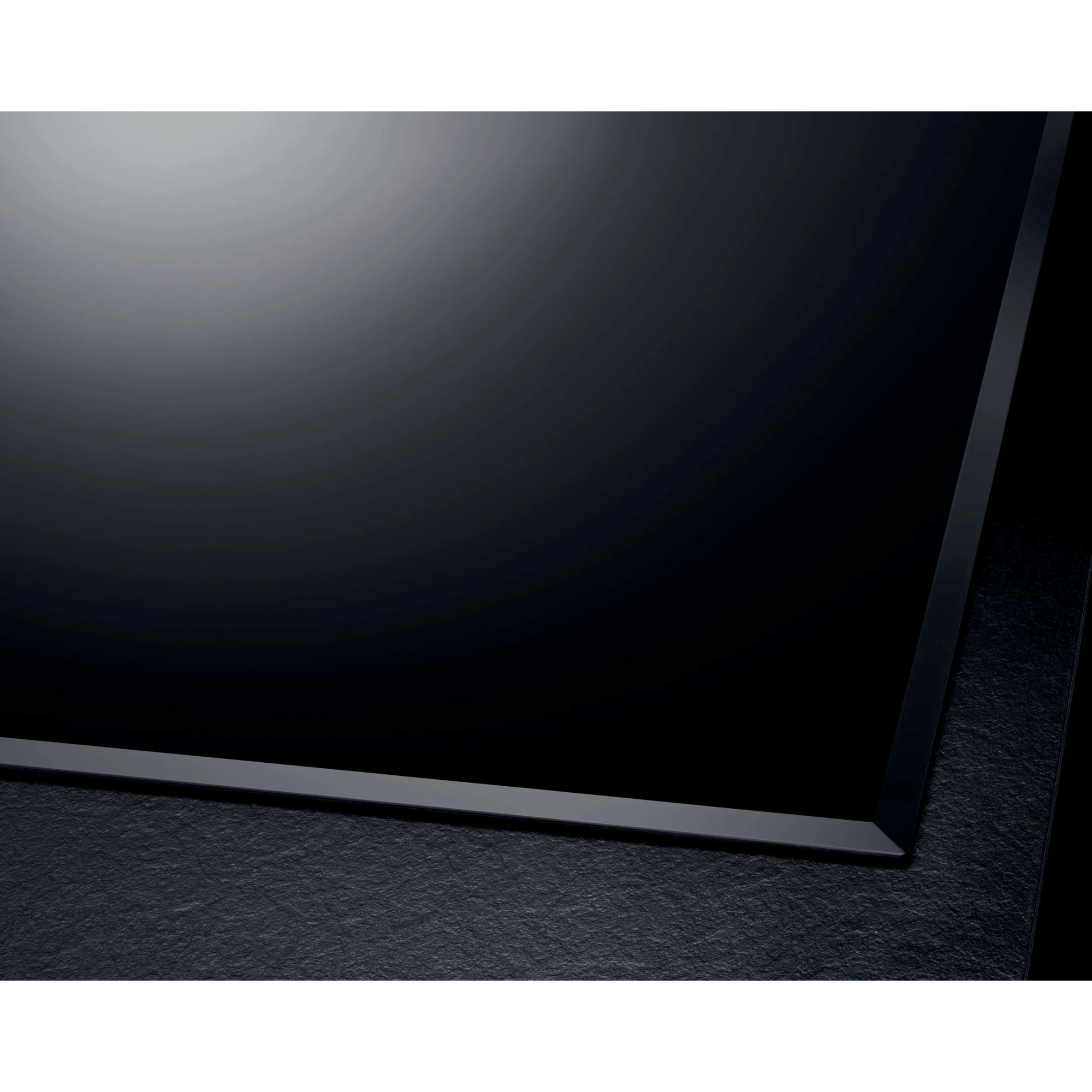 Shiny black cooktop with a matte frame on a textured surface.