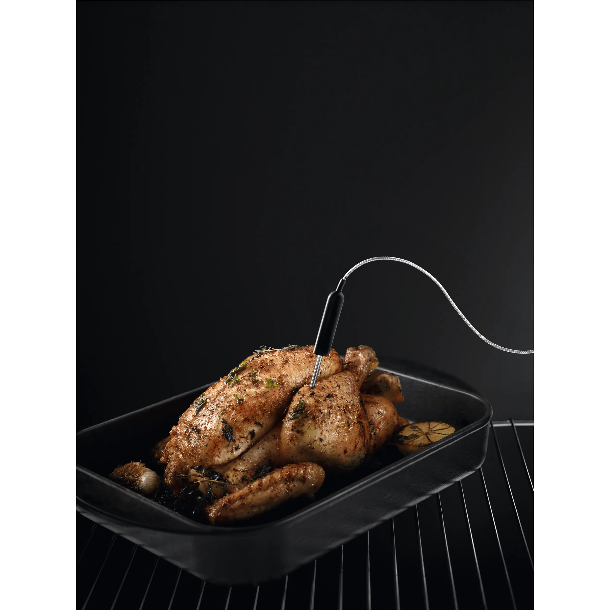 Un pollo arrosto con erbe e limone in una padella nera con termometro per carne.