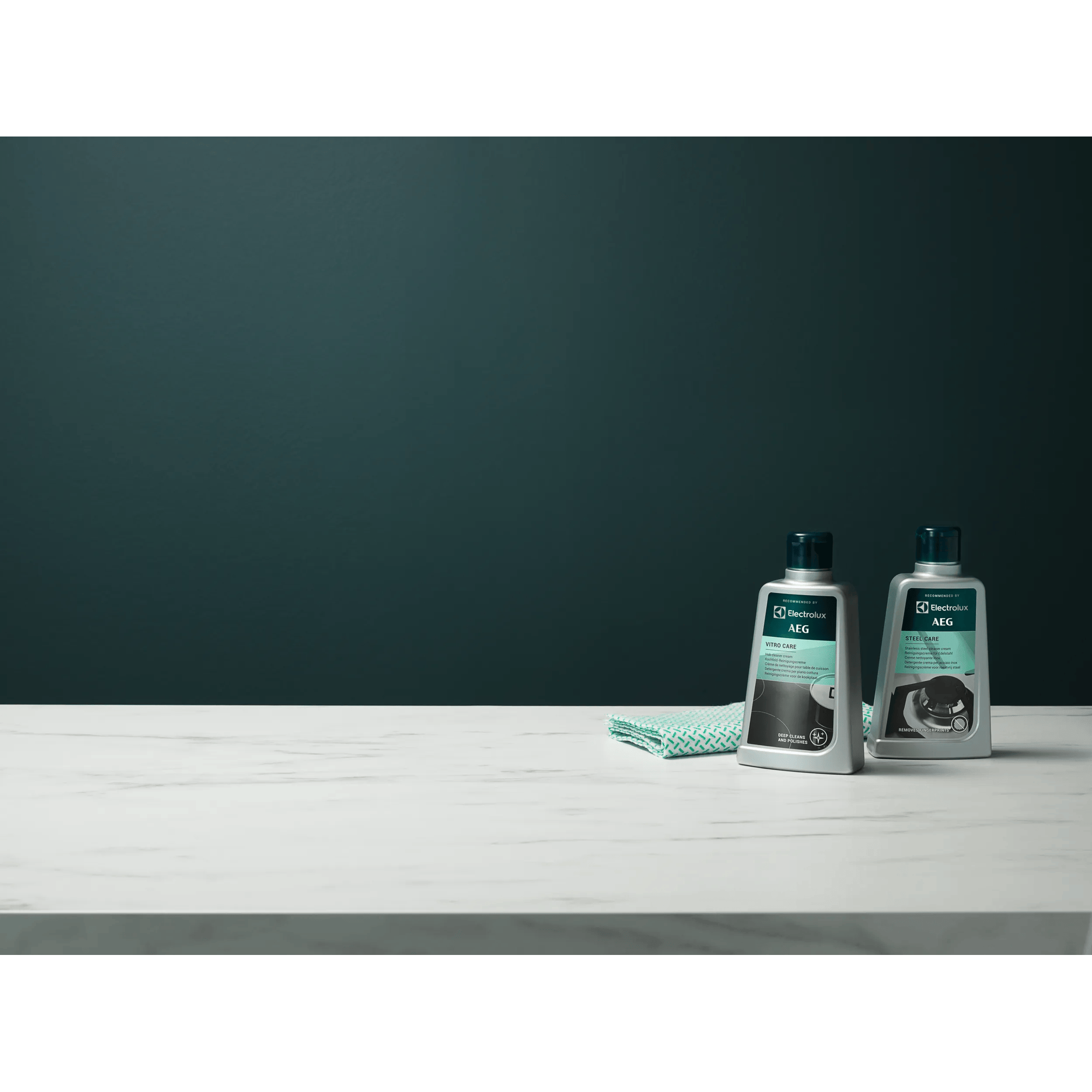 Dos botellas de limpiador AEG, una para vitrocerámica, otra para acero, sobre mesa mármol.