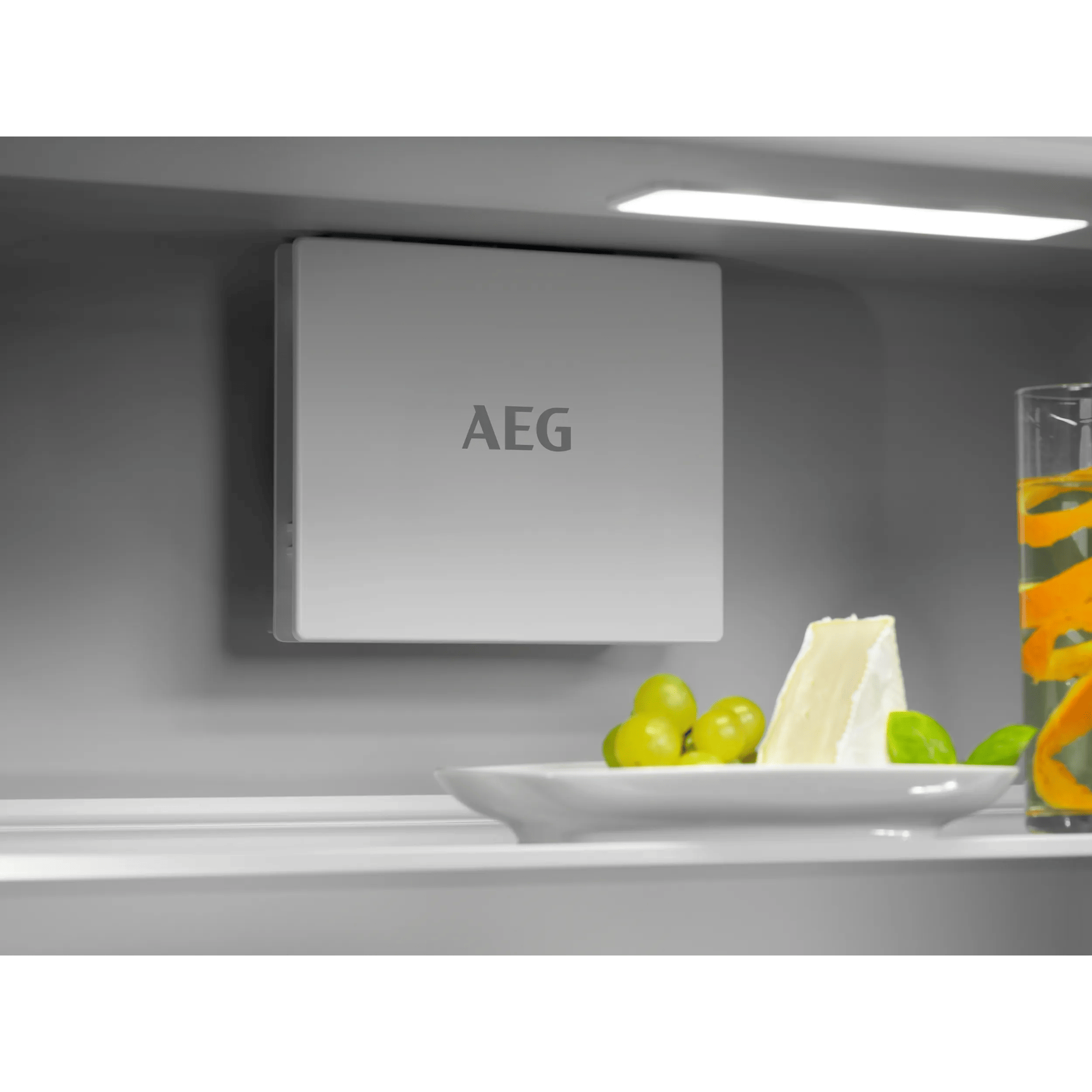 Un aparato AEG sobre un plato con queso, uvas y un vaso de bebida.