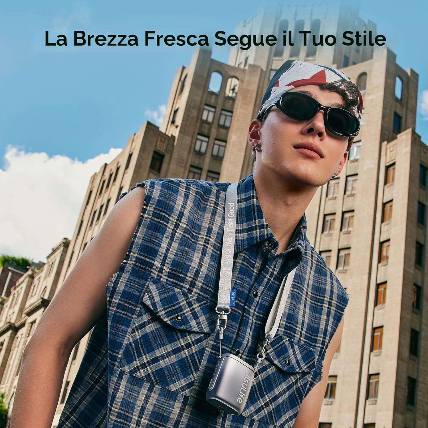 Un uomo con occhiali da sole e bandana, vestito con camicia a quadri, con un edificio dietro.